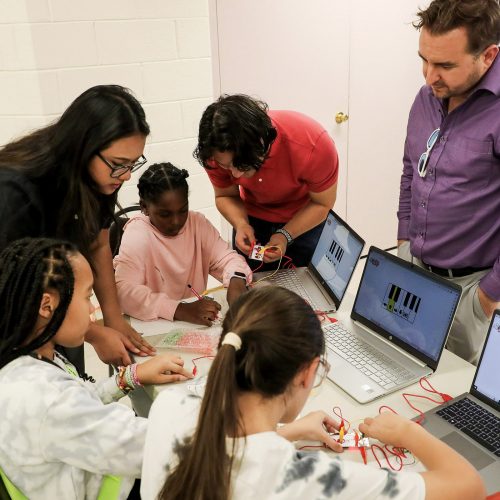 students and teachers gather around makey-makey electronic components and several laptops